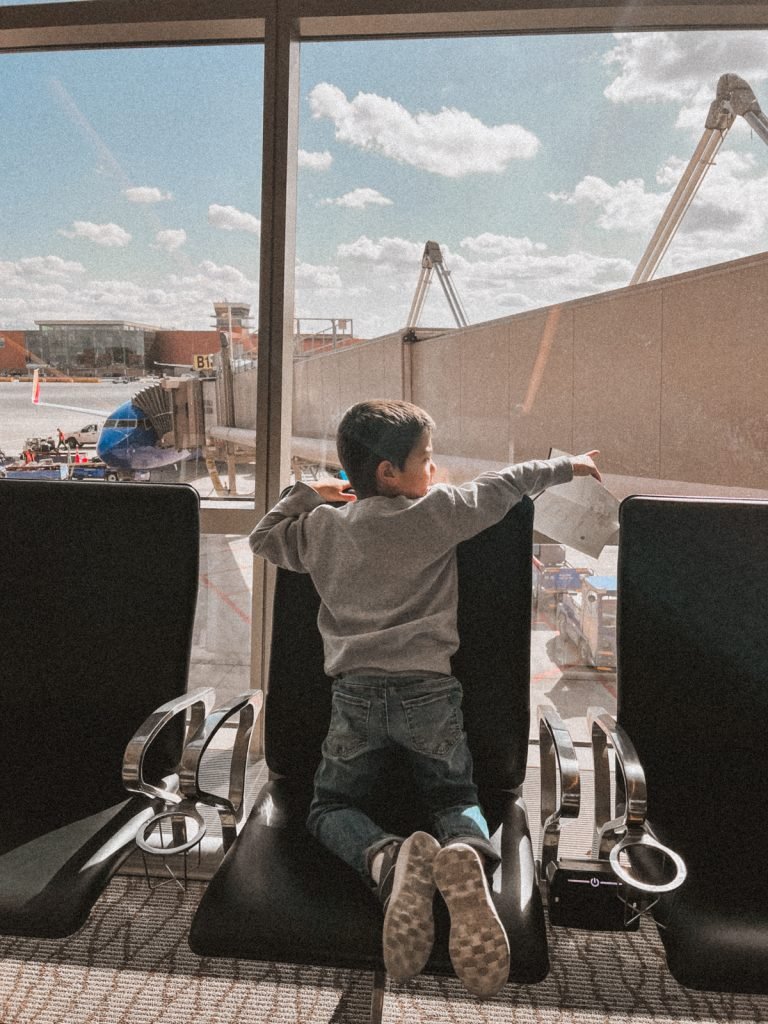 young boy in airport pointing in front of a window with airplane in the background